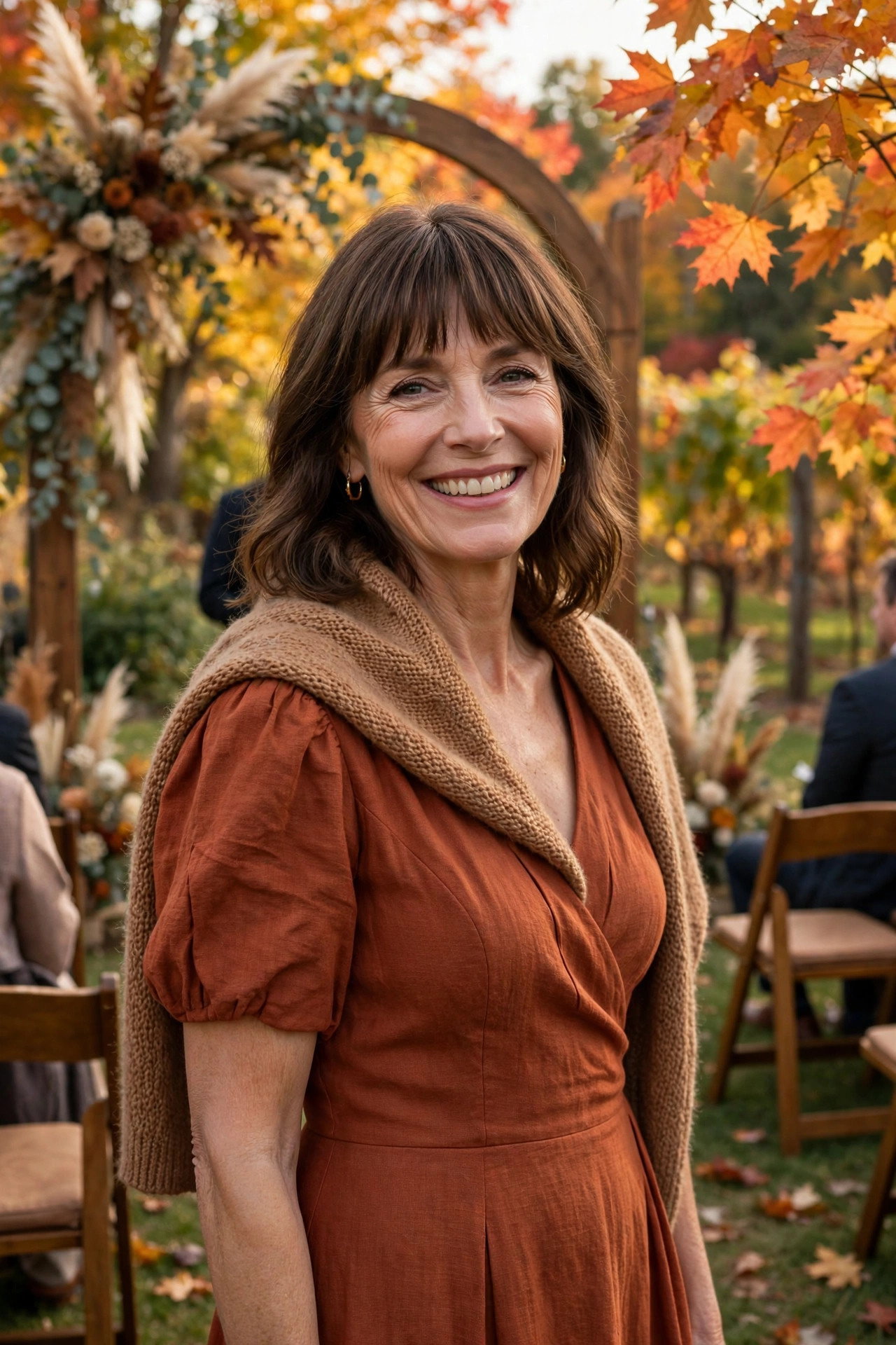 Woman in a rust-colored wrap dress with a knit shawl at an outdoor autumn wedding ceremony under a floral arch, a seasonal fall wedding guest dress.